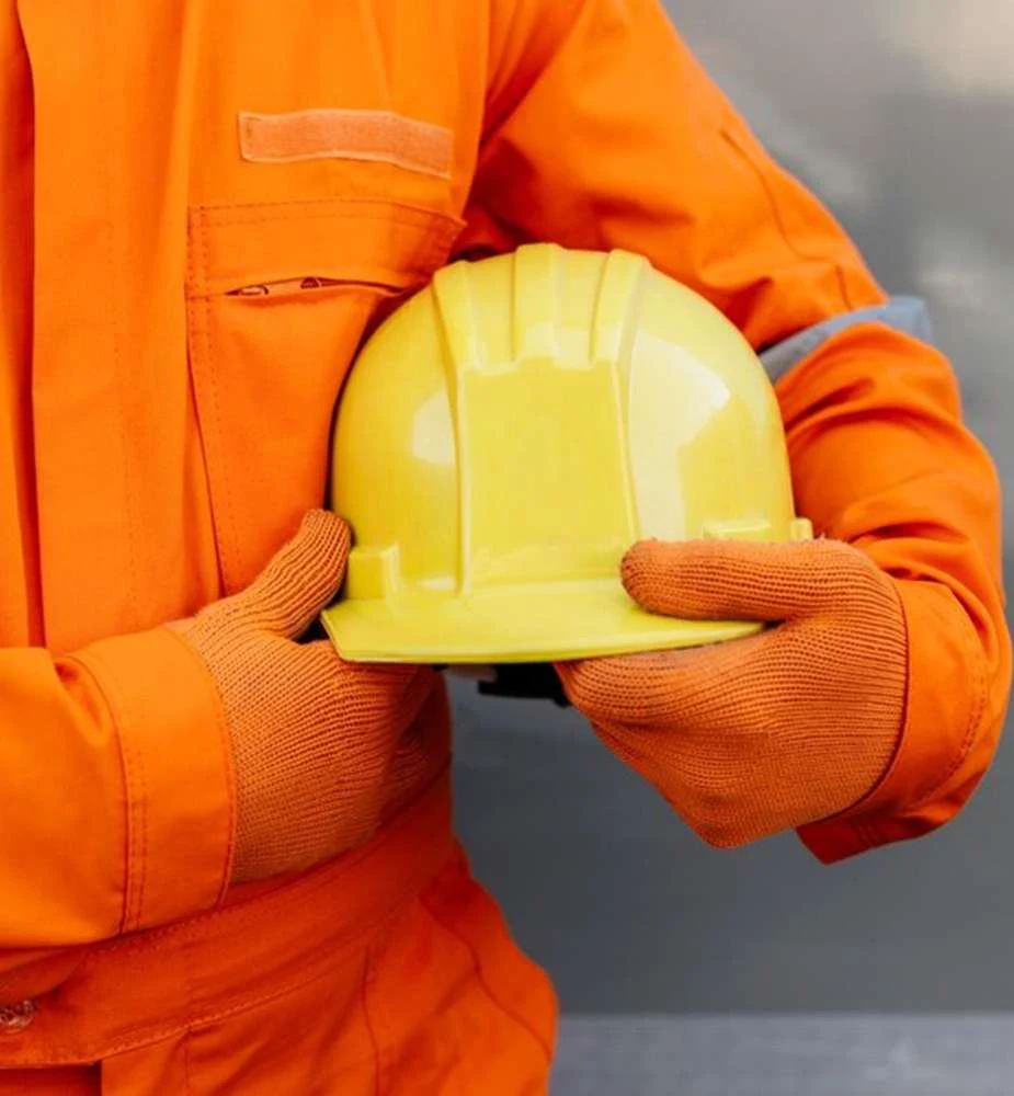 Profissional com uniforme laranja segurando um capacete de segurança amarelo, imagem do catálogo Ultra Safety